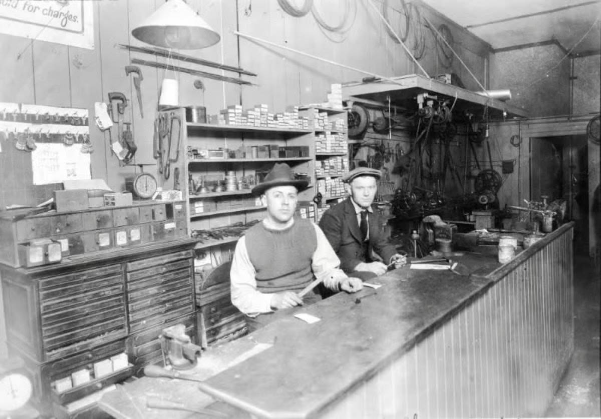 Archival photograph of the Central Key & Safe shop counter in its early years, with two men at the workbench